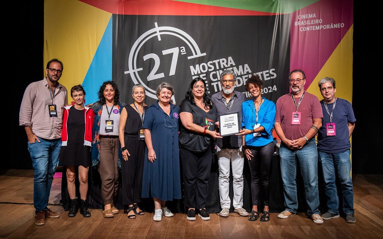 Autores da Carta Tiradentes posam para foto sobre palco, com o banner do Fesival de Cinema de Tiradentes ao fundo.